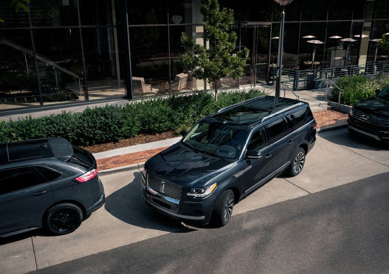 A 2024 Lincoln Navigator® SUV is being parallel parked between two vehicles on a downtown street outside of a luxury hotel.