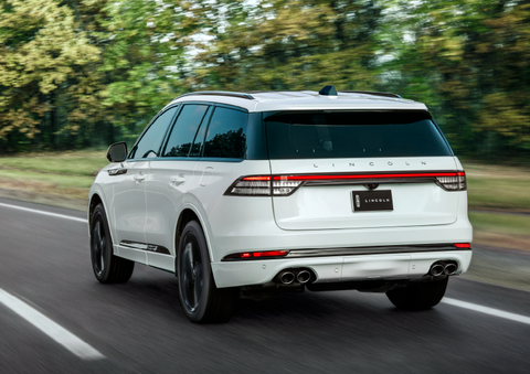 A white 2025 Lincoln Aviator® SUV is being driven away down a road lined with colorful trees. | Allan Vigil Lincoln, Inc. in Morrow GA