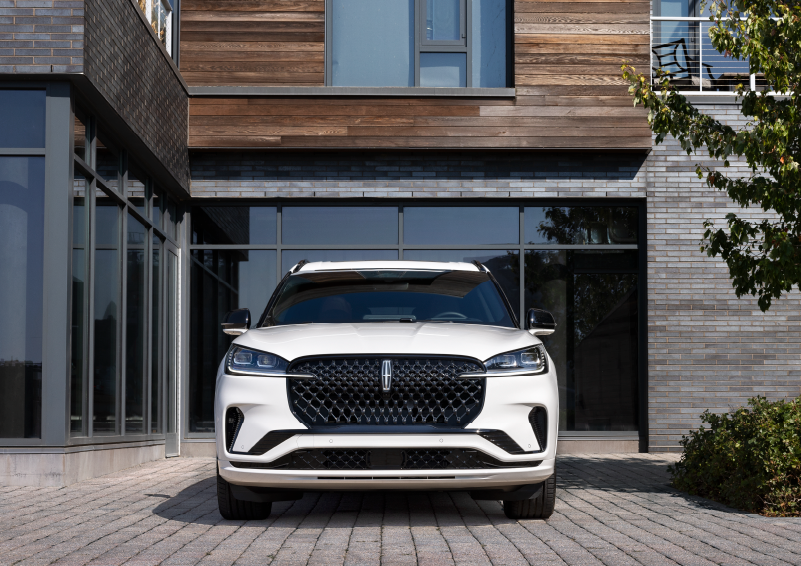 A white 2025 Lincoln Aviator® SUV is shown parked outside a modern building with gray brick and wood accents. | Allan Vigil Lincoln, Inc. in Morrow GA