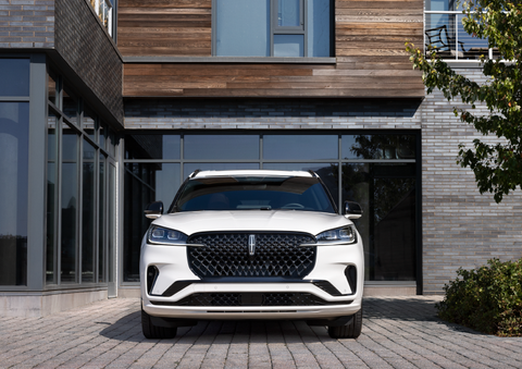 A white 2025 Lincoln Aviator® SUV is shown parked outside a modern building with gray brick and wood accents. | Allan Vigil Lincoln, Inc. in Morrow GA
