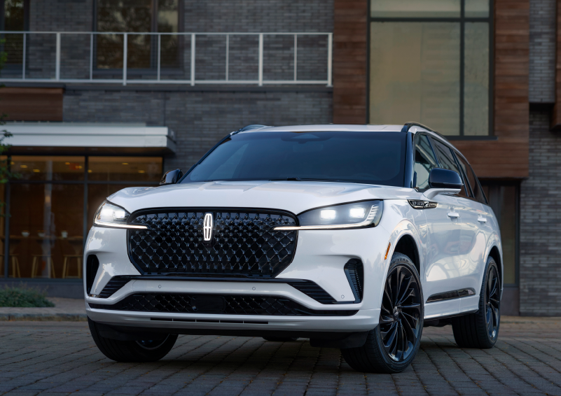 A white 2025 Lincoln Aviator® SUV is shown parked outside a modern building with gray brick and wood accents. | Allan Vigil Lincoln, Inc. in Morrow GA