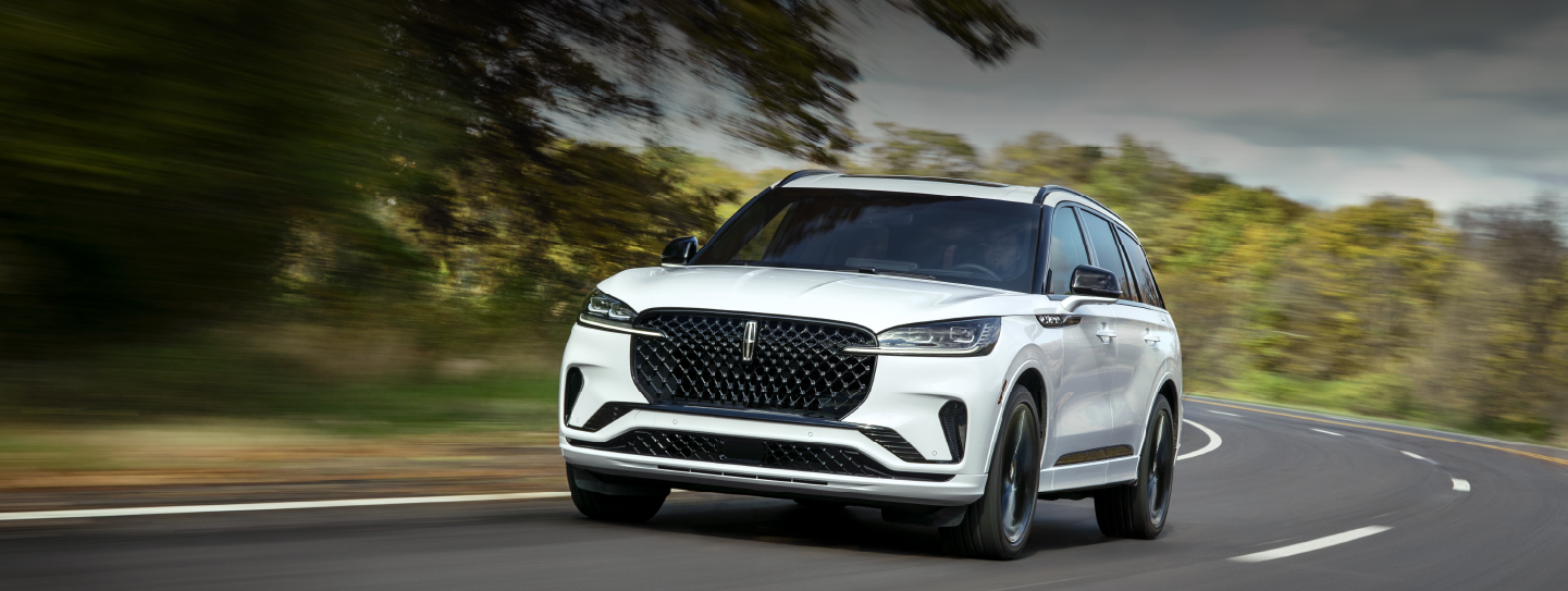 A white 2025 Lincoln Aviator® SUV is being driven down a road lined with trees. | Allan Vigil Lincoln, Inc. in Morrow GA