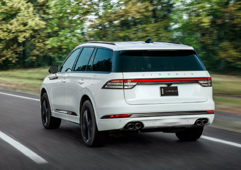 A white 2026 Lincoln Aviator® SUV is being driven away down a road lined with colorful trees. | Allan Vigil Lincoln, Inc. in Morrow GA