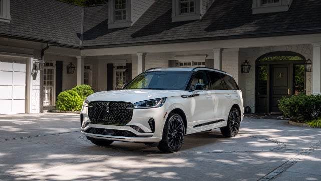 A white 2026 Lincoln Aviator® SUV is parked in the driveway of a luxury home. | Allan Vigil Lincoln, Inc. in Morrow GA