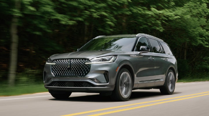 A 2027 Lincoln Aviator® SUV is being driven down a road lined with trees. | Allan Vigil Lincoln, Inc. in Morrow GA